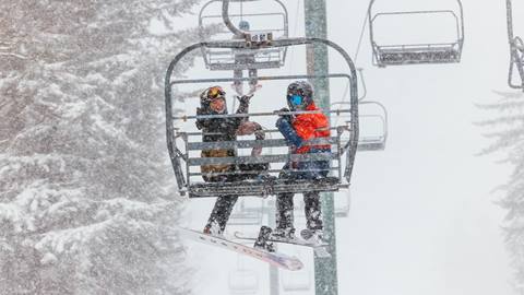 Two happy people waving while sitting on a chairlift in the snow